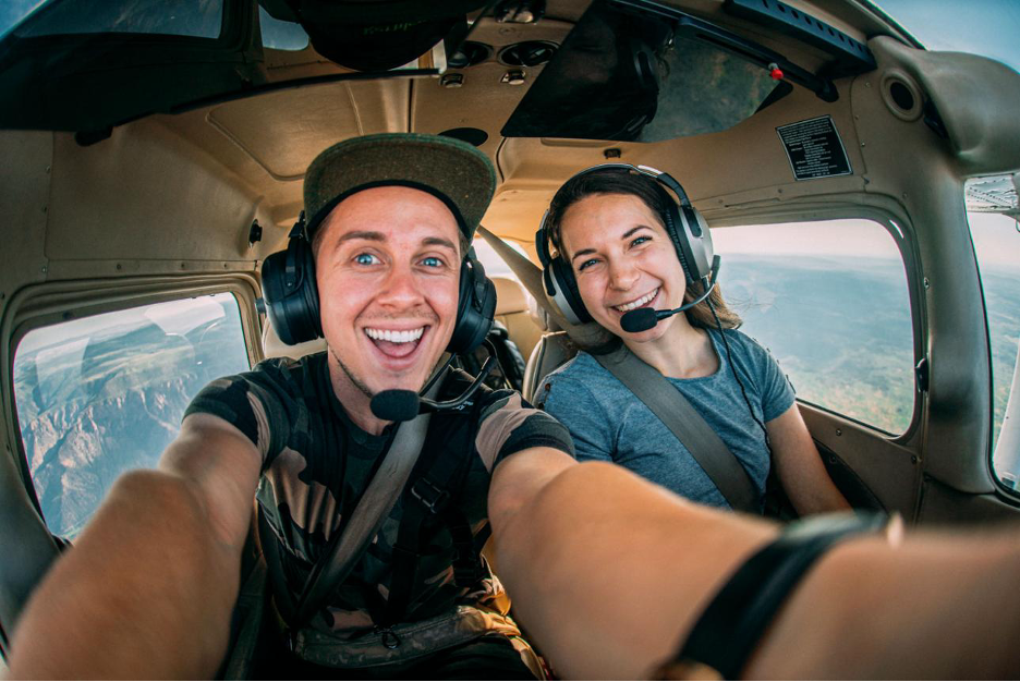 Two people grinning together inside a small aircraft cockpit.