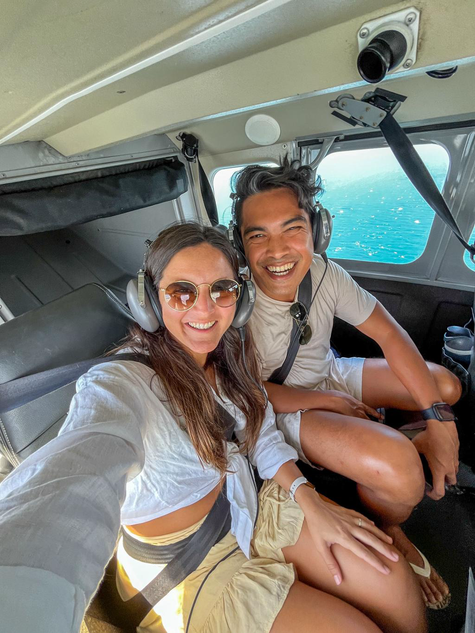 Pilots in headsets smiling on a seaplane over water.