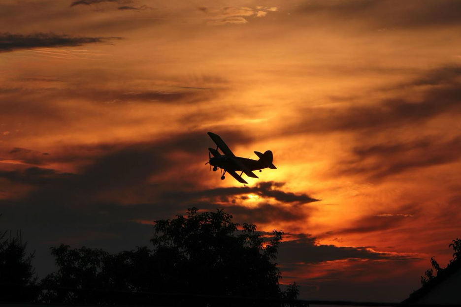 A biplane silhouetted against a calm sunset sky.